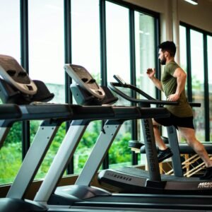 Young man workouts on treadmill in modern gym with large windows and natural light.