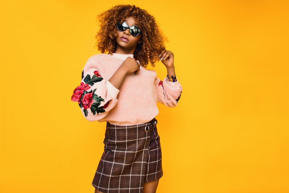 Chic woman with afro hair in a floral sweater and plaid skirt posing confidently.